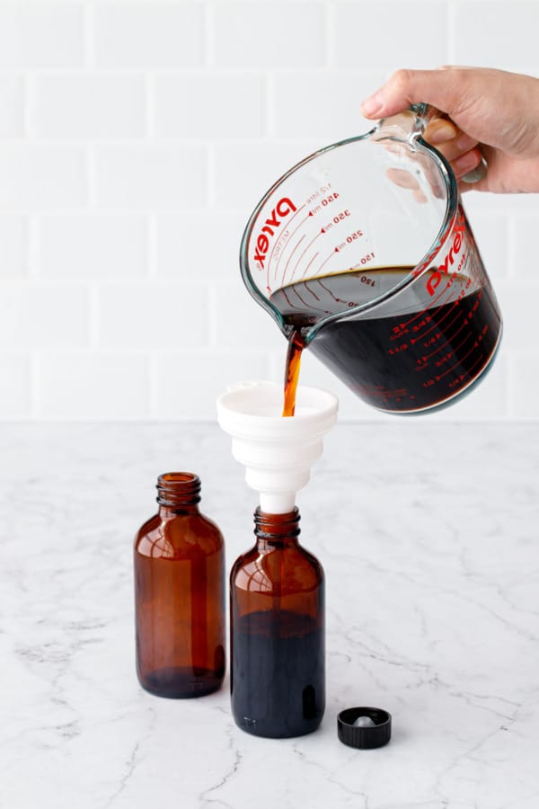 Pouring the final strained vanilla extract through a funnel into smaller 4oz amber glass bottles.