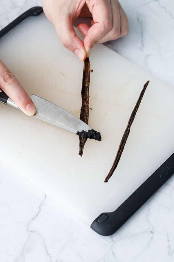 Using the back of the knife to scrape the seeds out of the split vanilla bean.
