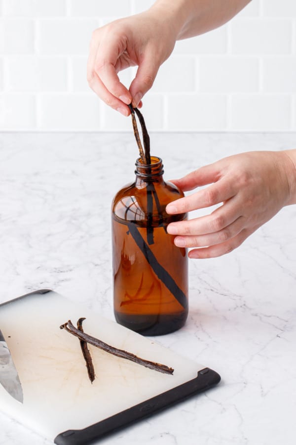 Placing the split and seeded vanilla bean pods into the bottle with the alcohol.