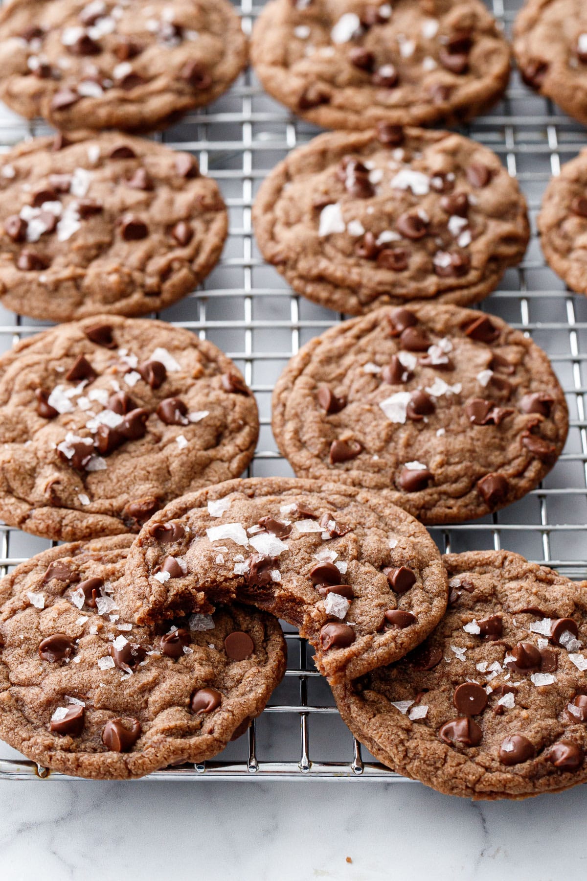Wire rack with rows of Nutella Chocolate Chip Cookies topped with flake sea salt, one cookie with a bite out of it sitting on top.
