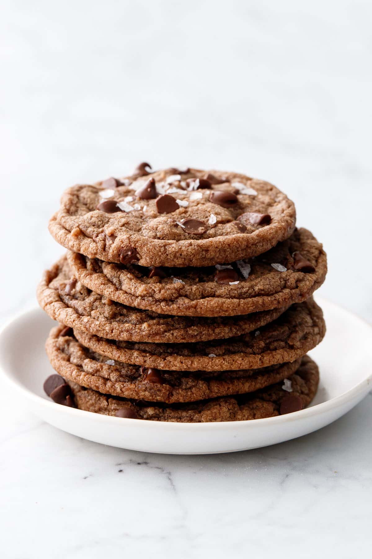 Stack of Nutella Chocolate Chip Cookies on a white plate and topped with visible flakes of sea salt.