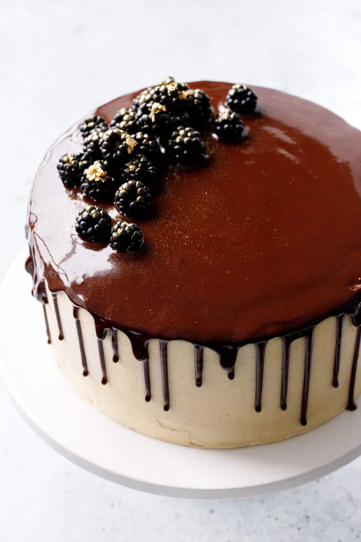 Blackberry Red Wine Chocolate Cake with shiny chocolate glaze dripping down the sides, with gold-dusted blackberries as decoration.