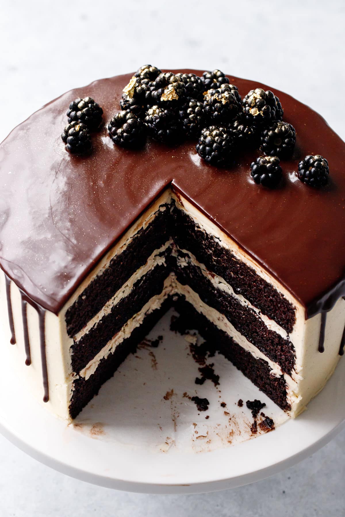 Blackberry Red Wine Chocolate Cake on a white cake stand with a perfect wedge cut out of it to showcase the distinct layers inside.