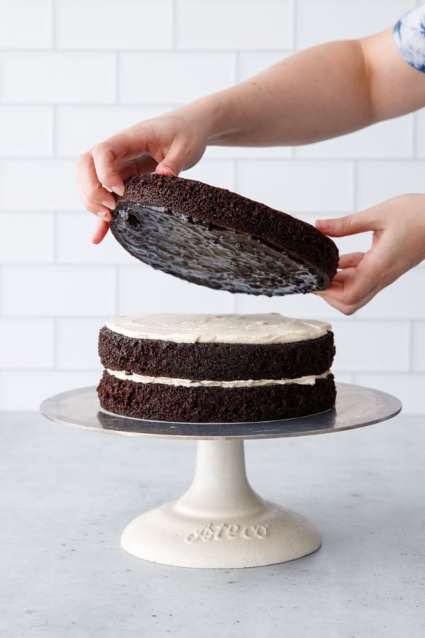 Assembling the cake layers, with jam spread on one cake layer being laid on top a layer of buttercream.