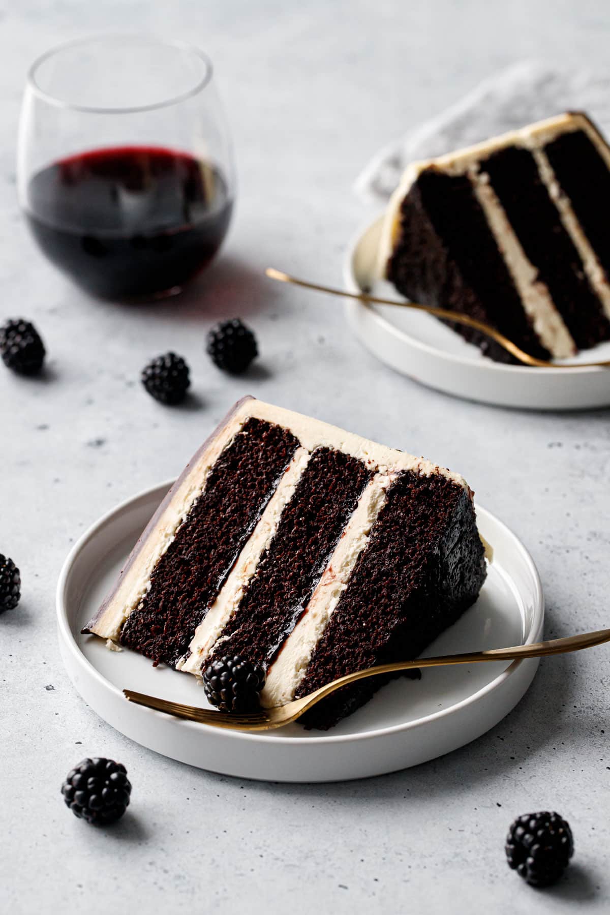 Closeup, slice of Blackberry Red Wine Chocolate Cake showing the distinct layers of dark cake, ivory buttercream, and blackberry jam in between.