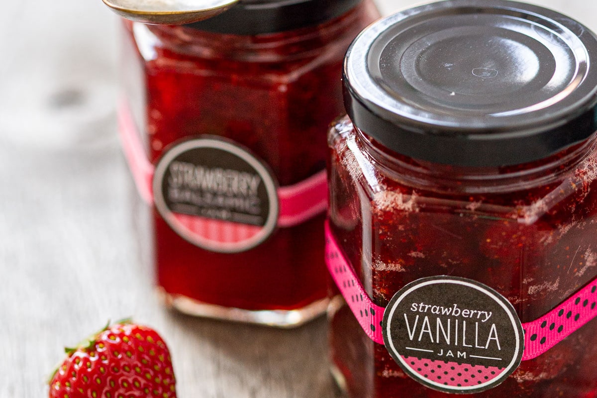 Jars of Strawberry Vanilla and Strawberry Balsamic Jam on a rustic wood background.