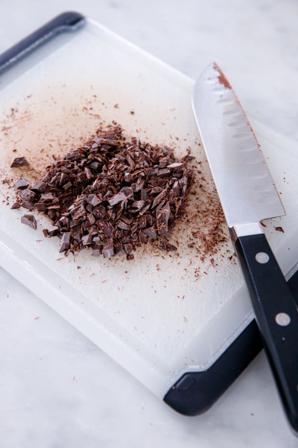 Knife laying on a cutting board next to a pile of finely chopped dark chocolate.