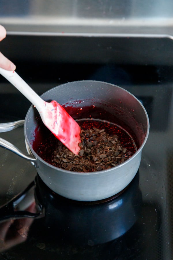 Stirring finely chopped chocolate into cooked raspberry jam.