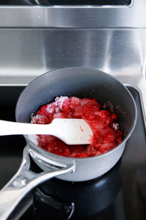 Stirring together raspberries, lemon juice and sugar in a saucepan on the stovetop.