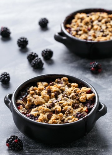 Two black baking dishes with Blackberry Chocolate Chip Cookie Crumble on a chalkboard background