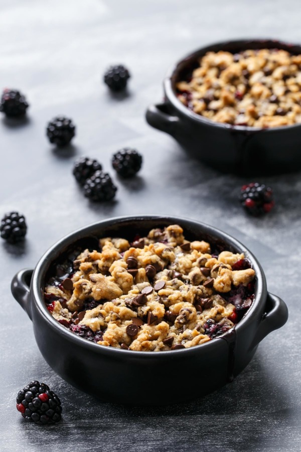 Two black baking dishes with Blackberry Chocolate Chip Cookie Crumble on a chalkboard background