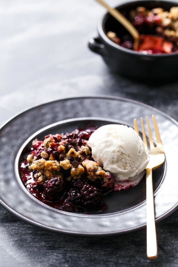 Serving of Blackberry Chocolate Chip Cookie Crumble on a black plate with scoop of vanilla ice cream