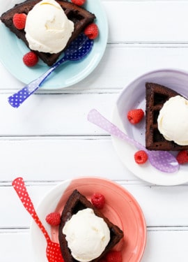 Overhead, three colorful plates each with a quarter chocolate waffle, with fresh berries and colorful plastic spoons.