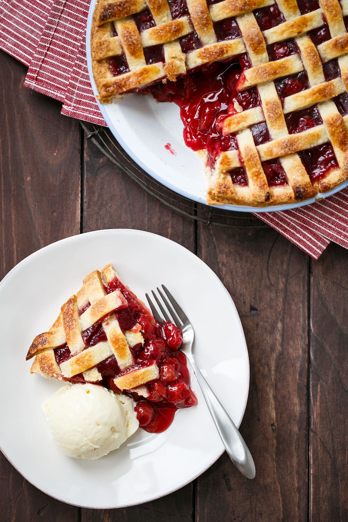 Overhead, Tart Cherry Pie with one slice cut out and sitting on a white plate with a fork and scoop of vanilla ice cream.