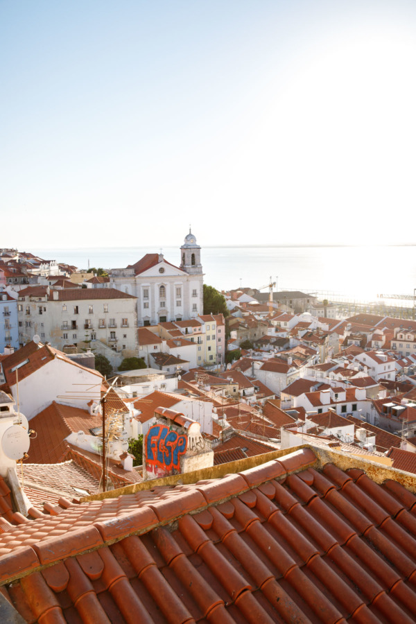 Looking out over the rooftops of the Alfama neighborhood in Lisbon, Portugal, with the Tagus river in the background.