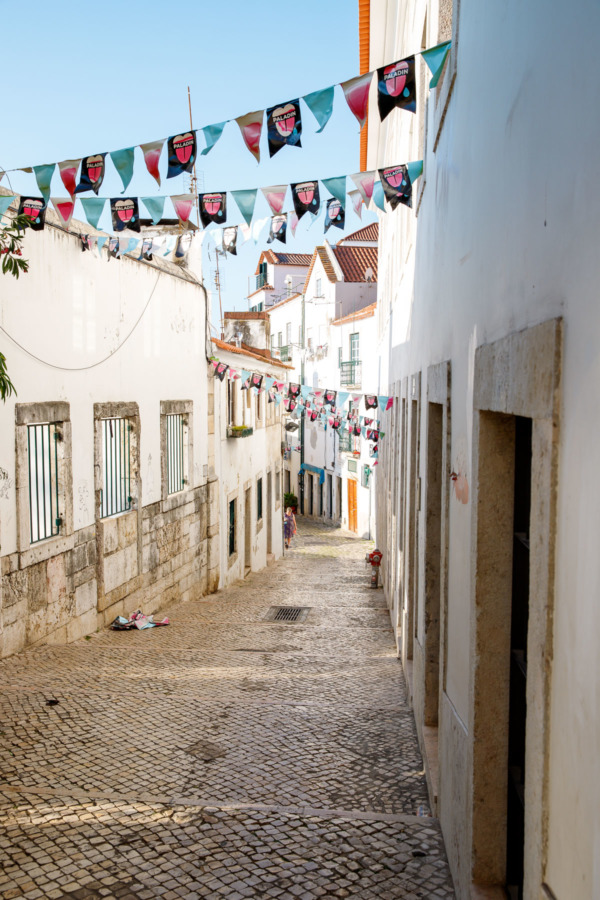 Narrow cobblestone street crisscrossed by colorful buntings in Lisbon, Portugal