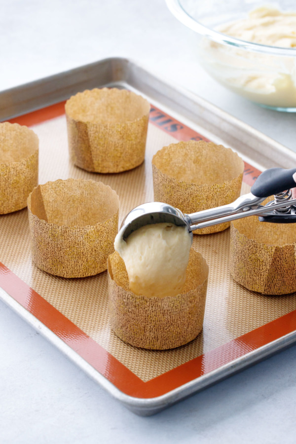 Using a large cookie scoop to portion the muffin batter into the baking papers.