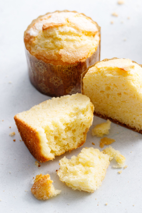 Two Portuguese rice muffins, one cut in half and partially eaten on a white background.