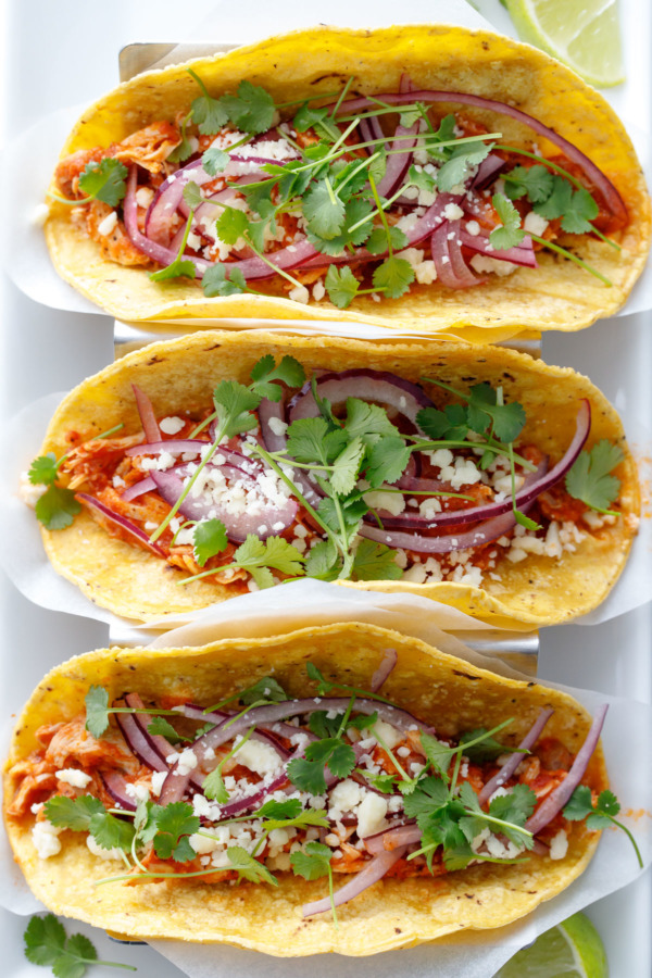 Overhead of three chicken tinga tacos topped with pickled red onion, crumbled cotija cheese, and fresh micro cilantro