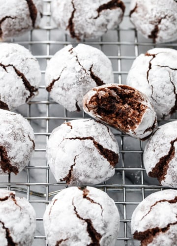 Rows of Chocolate Amaretti Cookies on a wire cooling rack, with one cookie with a bite taken out of it.