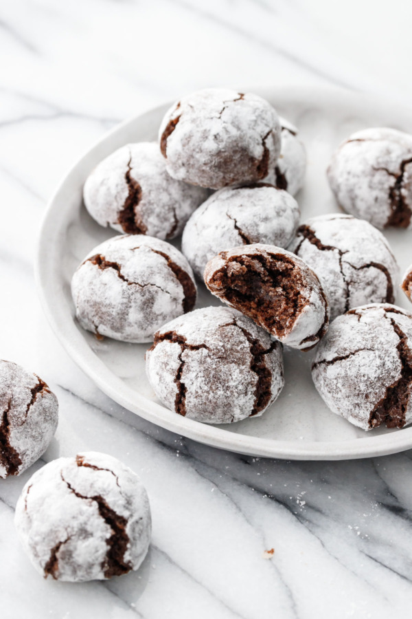 A plate piled high with powdered-sugar coated Chocolate Amaretti Cookies.