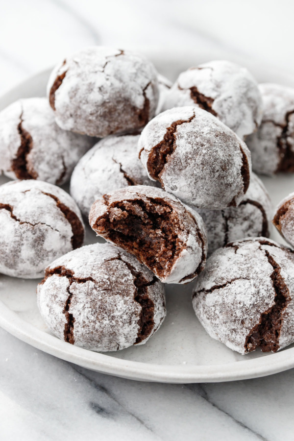 A plate full of Chocolate Amaretti Cookies, one cookie with a bite taken out of it.