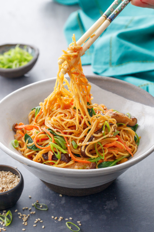 Sesame Stir Fry Noodles in a homemade ceramic bowl, being picked up with a pair of vintage chopsticks