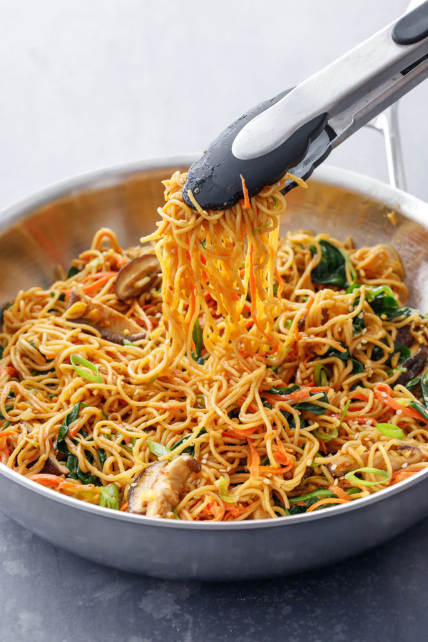 Saute pan with stir fry noodles being served with a pair of tongs