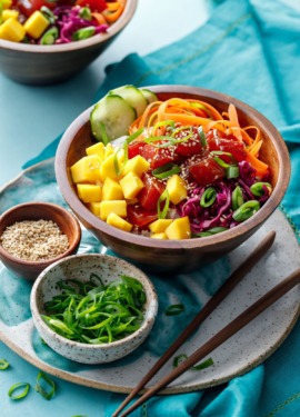 Ahi Mango Poke served in a wooden bowl on a turquoise background.