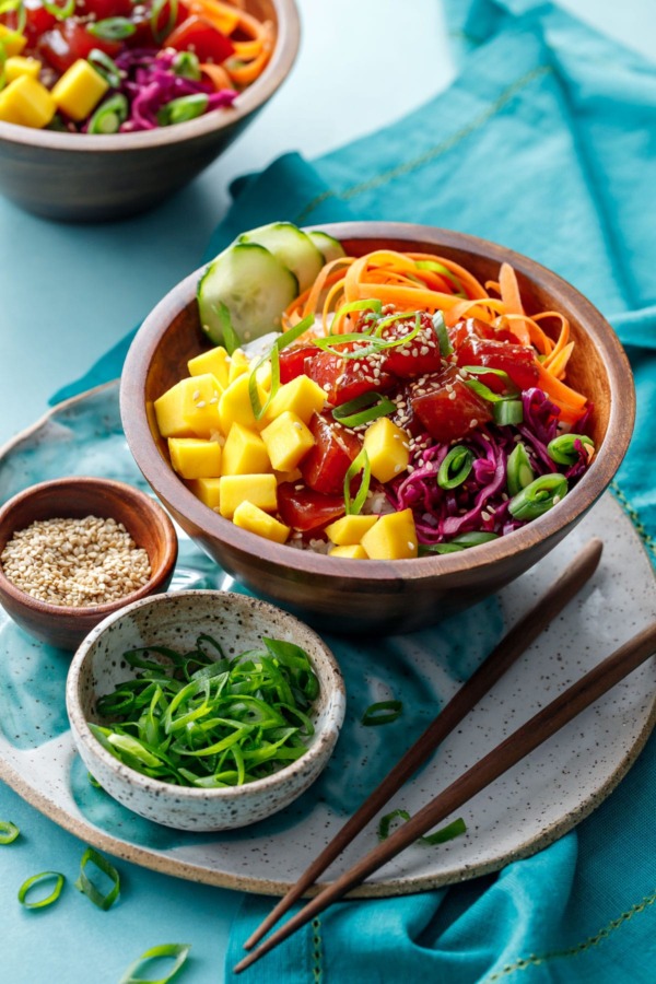 Ahi Mango Poke served in a wooden bowl on a turquoise background.