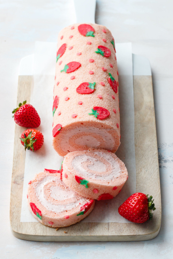 Japanese-inspired Spring Strawberry Cake Roll on a cutting board with fresh strawberries on the side.