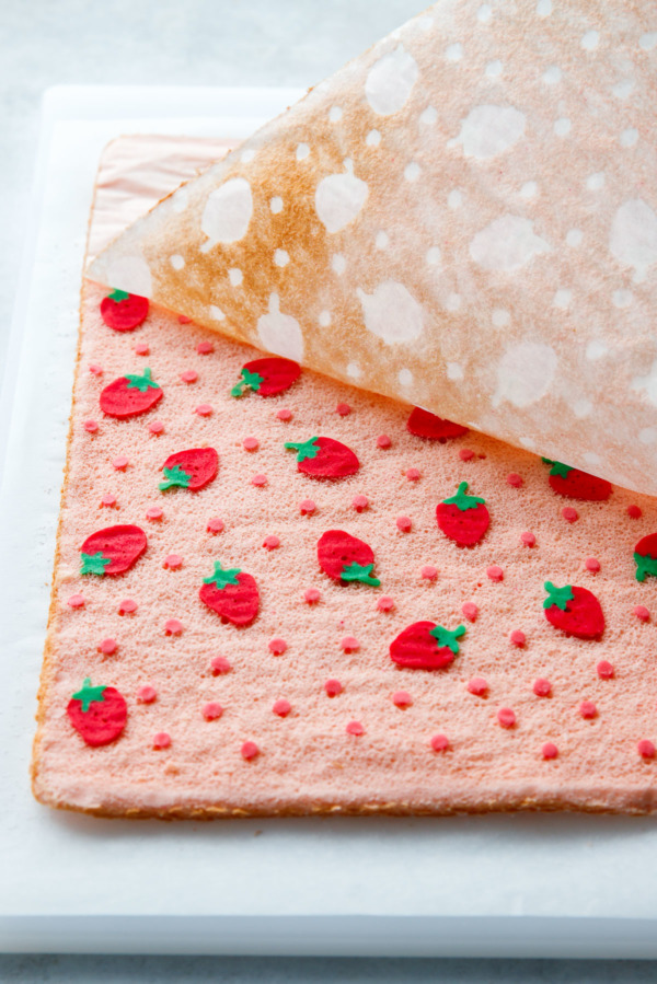 Peeling off the parchment paper to reveal the pink strawberry design on a Japanese-inspired cake roll