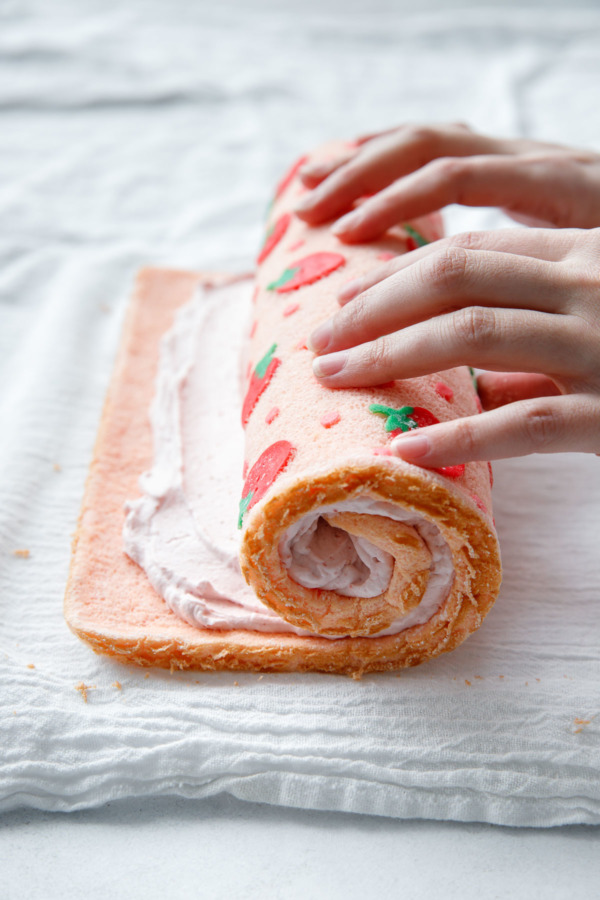 Rolling up the cake roll with the strawberry whipped cream filling.