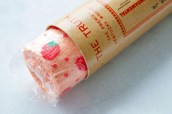 Final cake roll wrapped in plastic, fits perfectly inside a round whiskey bottle tube to hold its round shape.