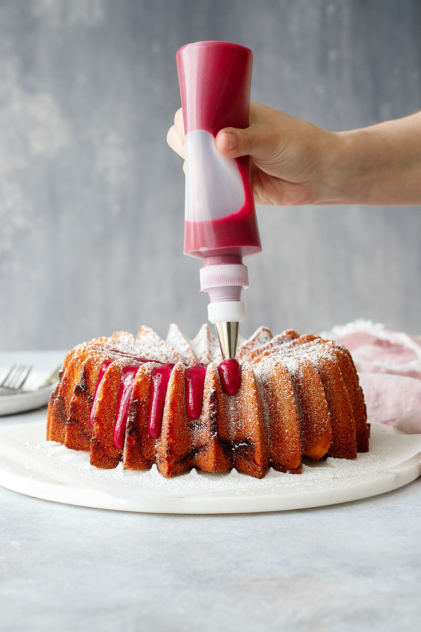 Piping a hot pink strawberry hibiscus glaze onto a bundt cake.