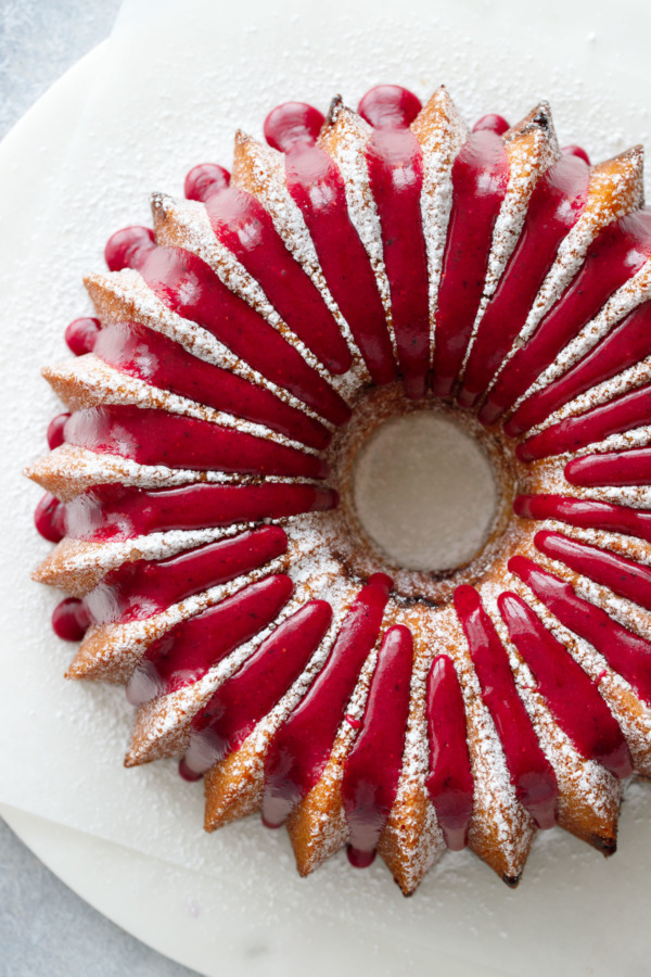 Top down view of a bundt cake, dusted with powdered sugar and drizzled with a bright pink strawberry hibiscus glaze.