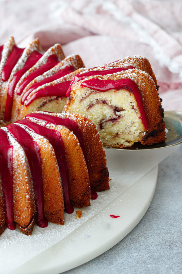 A slice of strawberry hibiscus swirl bundt cake with a bright pink strawberry hibiscus glaze.