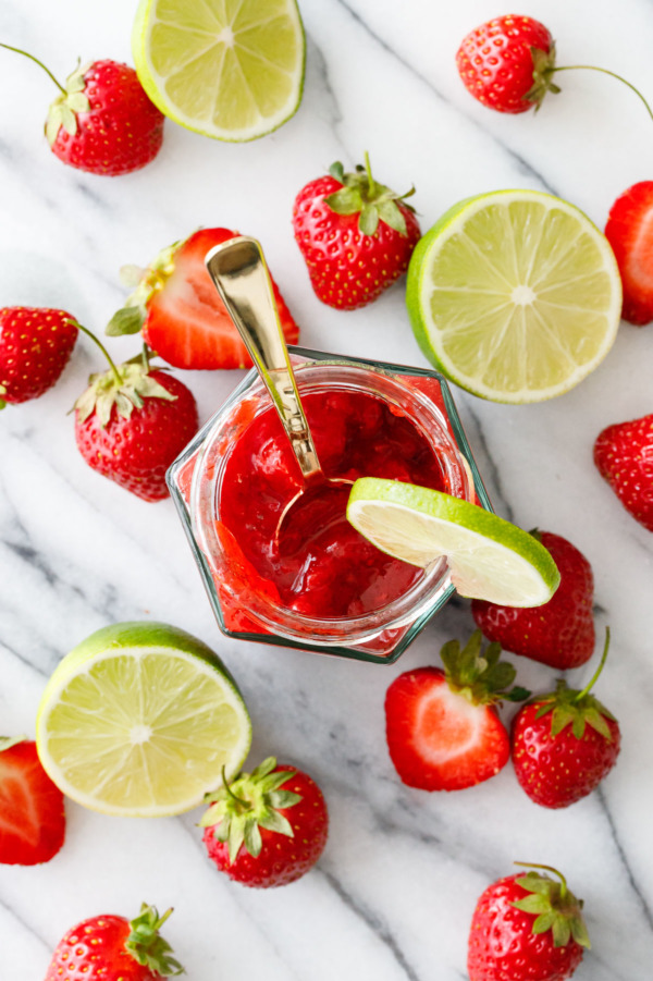Flat-lay shot of glass jars with Strawberry Margarita Jam and fresh strawberries and limes.