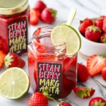 Homemade strawberry margarita jam in hexagon glass jars with custom designed labels, surrounded by fresh strawberries and limes.