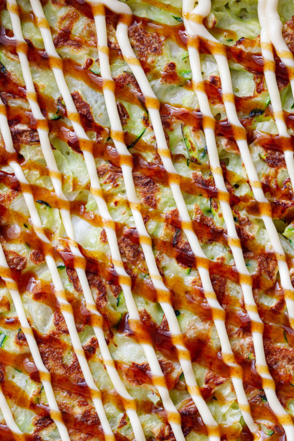 Close up of Cabbage & Zucchini Okonomiyaki, drizzled with kewpie mayo and okonomi sauce in a criss-cross pattern