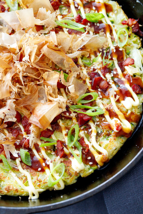 Close up of Cabbage & Zucchini Okonomiyaki cooked in a cast iron skillet, topped with bonito flakes.