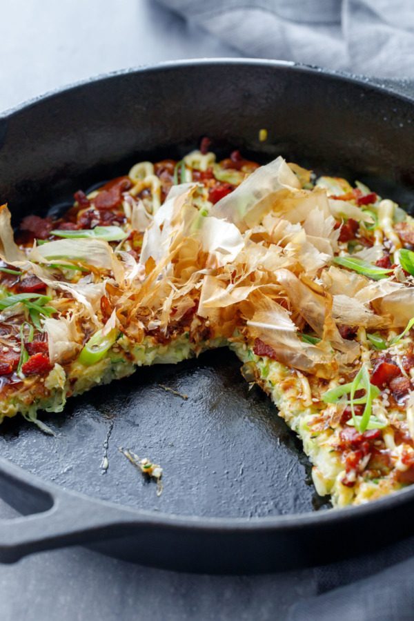 A cast iron skillet with Cabbage & Zucchini Okonomiyaki with a slice cut out of it.