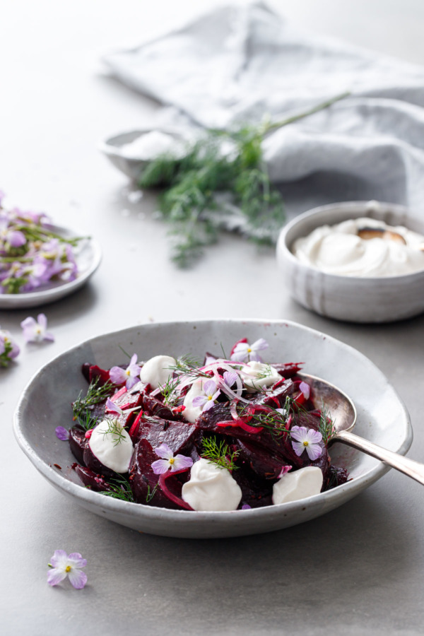 Handmade ceramic bowl filled with cumin-spiced beet salad with bowls of yogurt and radish flowers on the side