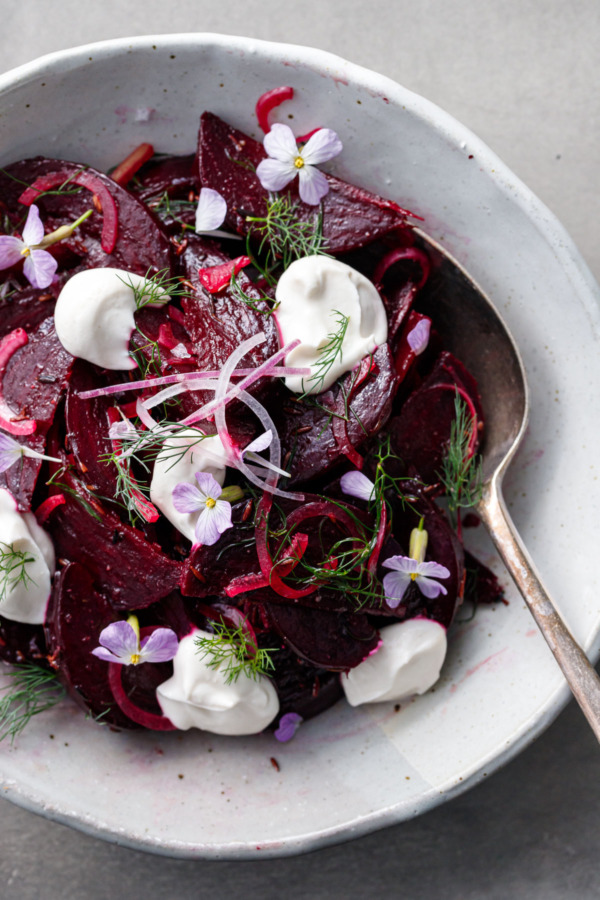 Closeup of a cumin-spiced beet salad, with dollops of greek yougurt, fresh dill and purple radish flowers scattered on top