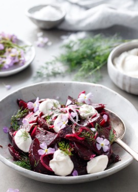 Handmade ceramic bowl filled with cumin-spiced beet salad with bowls of yogurt and radish flowers and fresh dill in the background