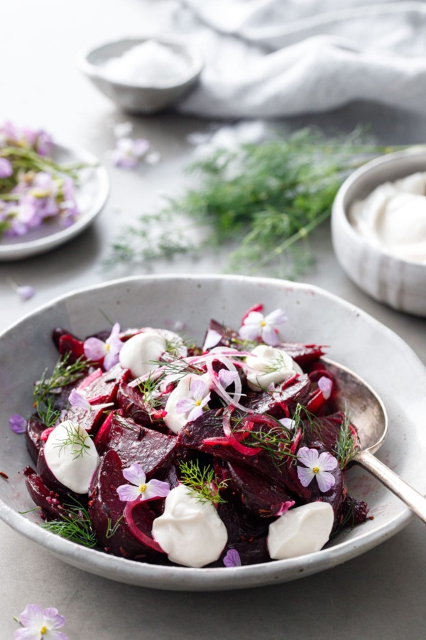 Handmade ceramic bowl filled with cumin-spiced beet salad with bowls of yogurt and radish flowers and fresh dill in the background