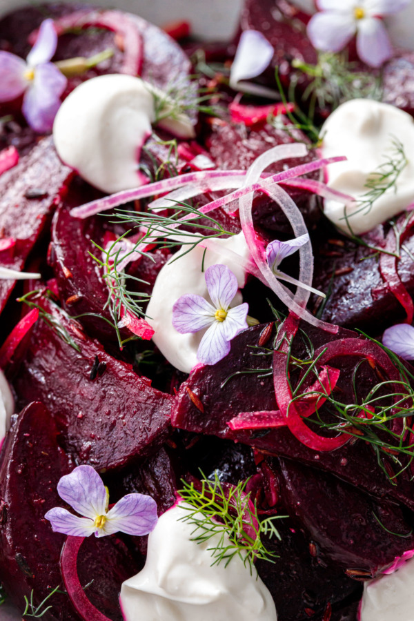 Closeup of a cumin-spiced beet salad, with dollops of greek yougurt, fresh dill and purple radish flowers scattered on top