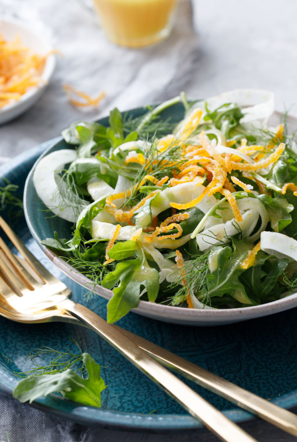 Fennel and Arugula Salad with Candied Orange Peel, served in a Handmade ceramic bowl with gold flatware.