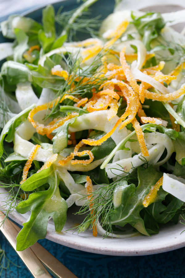 Close up shot of a bowl of Fennel and Arugula Salad with Candied Orange Peel and drizzled with orange vinaigrette.