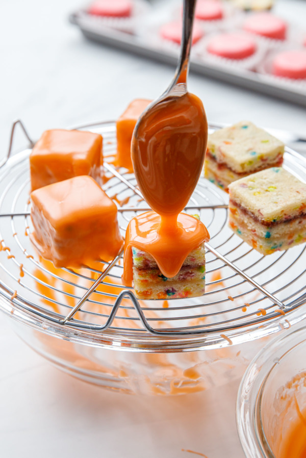 Glazing individual petit fours cakes with an orange colored poured fondant glaze.